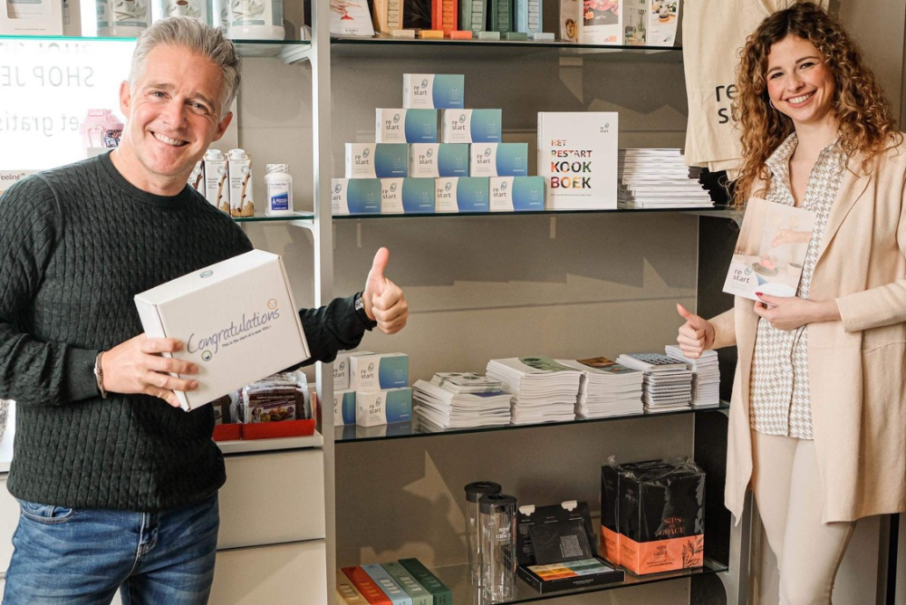 Twee mensen glimlachen en tonen gezonde lifestyle producten, kookboeken en supplementen in winkel.