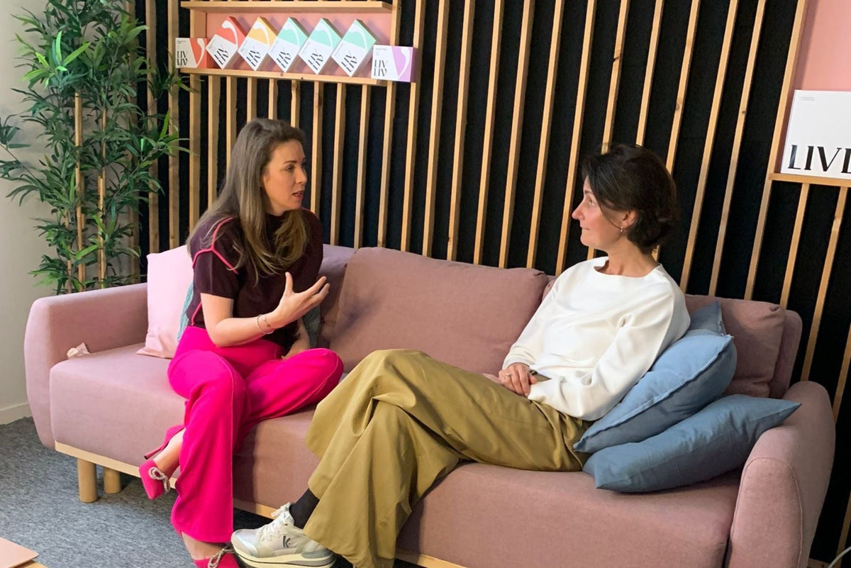Twee vrouwen in gesprek op een roze bank, ontspannen setting over gezonde levensstijl coaching.