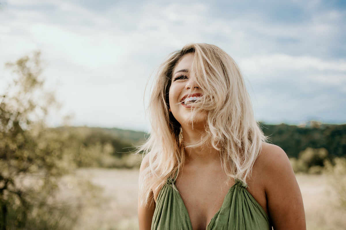 Vrolijke jonge vrouw met blond haar lacht buiten in de natuur, gezonde levensstijl sfeer